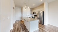 Located at 5001 State Highway 114 in Northlake, Texas, this single-story, one-bedroom, one-bathroom residence offers a thoughtfully designed layout with contemporary finishes throughout. Wood-look plank flooring flows consistently across all living areas, contributing to a clean, cohesive aesthetic.

The kitchen serves as a central highlight, featuring granite countertops, crisp white cabinetry, and a full suite of stainless steel appliances including a range, over-the-range microwave, and refrigerator. A kitchen island with an undermount sink and pendant lighting above adds both functionality and style, while recessed lighting illuminates the space efficiently.

The bedroom is a comfortable, naturally lit retreat with multiple windows fitted with horizontal blinds, a ceiling fan, and direct access to the bathroom. The bathroom continues the granite countertop theme with a white vanity, framed mirror, and a glass-enclosed shower/tub combination, maintaining the home's consistent modern finishes.

A hallway connects the key areas of the home and leads to the front entry. The open-concept flow between the kitchen and living areas maximizes the usable space and enhances the overall sense of openness. Neutral wall tones throughout create a versatile backdrop suitable for a variety of interior styles.