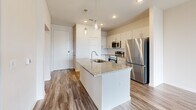 Located at 5001 State Highway 114 in Northlake, Texas, this single-story, one-bedroom, one-bathroom residence offers a thoughtfully designed layout with contemporary finishes throughout. Wood-look plank flooring flows consistently across all living areas, contributing to a clean, cohesive aesthetic.

The kitchen serves as a central highlight, featuring granite countertops, crisp white cabinetry, and a full suite of stainless steel appliances including a range, over-the-range microwave, and refrigerator. A kitchen island with an undermount sink and pendant lighting above adds both functionality and style, while recessed lighting illuminates the space efficiently.

The bedroom is a comfortable, naturally lit retreat with multiple windows fitted with horizontal blinds, a ceiling fan, and direct access to the bathroom. The bathroom continues the granite countertop theme with a white vanity, framed mirror, and a glass-enclosed shower/tub combination, maintaining the home's consistent modern finishes.

A hallway connects the key areas of the home and leads to the front entry. The open-concept flow between the kitchen and living areas maximizes the usable space and enhances the overall sense of openness. Neutral wall tones throughout create a versatile backdrop suitable for a variety of interior styles.