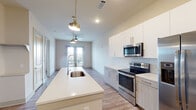 This well-appointed one-bedroom, one-bathroom residence in Memphis, TN offers a thoughtfully designed open-concept layout with contemporary finishes throughout. The kitchen serves as the centerpiece of the living space, showcasing a large quartz-topped island with an undermount sink and pendant lighting overhead. White upper cabinetry pairs elegantly with two-tone lower cabinets, while a herringbone tile backsplash adds a refined touch. A full suite of stainless steel appliances — including a side-by-side refrigerator, electric range, and over-the-range microwave — completes the functional and stylish kitchen. Wood-look flooring flows seamlessly throughout the entire unit, complementing the clean, neutral color palette. The living area benefits from natural light streaming through glass French doors, with a ceiling fan adding comfort. The bedroom is generously sized with a large window framing views of the surrounding Memphis cityscape. The bathroom features a granite-topped vanity with ample drawer storage and a glass-enclosed walk-in shower. Recessed lighting and ceiling fans throughout the unit contribute to a bright, comfortable ambiance, making this an ideal modern urban residence.