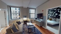 Located at 175 N Wabash Avenue in Chicago's vibrant Loop neighborhood, this well-appointed single-floor unit offers a thoughtfully designed layout with modern finishes throughout. The living area is a standout space, featuring soaring ceilings, warm hardwood flooring, and two large windows that frame views of the surrounding city architecture, flooding the room with natural light. A plush sofa, marble-top coffee table, accent chair, and a sleek media console complete the inviting setup.

The kitchen is fully equipped with rich cherry wood cabinetry, granite countertops, a tile backsplash, and full-size black appliances including a refrigerator, stove, microwave, and dishwasher. A central island provides additional prep space and casual seating.

The primary bedroom features a patterned accent wall, carpeted flooring, and a large window with urban views, accompanied by a full-length mirror and tasteful lighting. The second bedroom is bright and comfortable, with city skyline views and carpeted floors. Two bathrooms serve the unit — one with a vessel sink vanity and tile flooring, and another with a glass-enclosed walk-in shower — both finished in clean, neutral tones. The overall ambiance is contemporary and functional, ideal for urban living in the heart of Chicago.