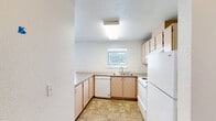 Located at 12623 E Broadway Ave in Spokane Valley, WA, this two-bedroom, one-bathroom unit offers a practical and well-organized single-floor layout. The combined kitchen and living area forms the heart of the home, featuring light wood cabinetry, a smooth countertop peninsula that separates the kitchen from the living space, a white appliance suite including a range and refrigerator, and a window that brings in natural light. The living room features neutral-toned carpet, a wall-mounted air conditioning unit, and multiple windows dressed with vertical blinds, allowing ample natural light. A door leads directly to an outdoor area, adding a convenient connection to the exterior. The two bedrooms are carpeted and finished with clean white walls and textured ceilings. The primary bedroom is cozy and functional, while the second bedroom features a wide window with blinds and a baseboard heater. A dedicated closet provides organized storage, complete with wire shelving. The full bathroom includes a vanity with under-sink cabinetry, a large mirror with overhead lighting, a tub/shower combination with tile surround, and tile flooring. An additional closet space off one of the bedrooms provides utility storage. Overall, the unit presents a clean, straightforward design suited for comfortable everyday living.