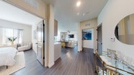Located at 7701 Interbay Blvd in Tampa's 33616 zip code, this single-floor residence offers a thoughtfully designed open-concept layout with contemporary finishes throughout. Dark wood-style flooring runs continuously across the living areas, creating a cohesive and polished aesthetic. The entryway provides a welcoming introduction to the space, opening toward a well-appointed kitchen and a bright living area beyond. The kitchen features light wood cabinetry, a white subway tile backsplash, stainless steel appliances including a French door refrigerator, electric range, microwave, and dishwasher, along with a built-in pantry for additional storage. The open living and dining area is bathed in natural light from multiple windows dressed with blinds and sheer curtains, and is anchored by a ceiling fan overhead. The bedrooms offer a calm, neutral palette with ample natural light from well-placed windows. The primary bedroom includes distinctive wall décor and generous space for furnishings. Two bathrooms serve the residence — one featuring a granite-topped vanity with modern cabinetry, and the other offering a full tub-shower combination with large-format tile surround. Throughout, matte black hardware and clean architectural lines lend the home a modern, cohesive character.