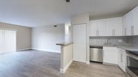 This single-floor residence presents a thoughtfully designed open-concept layout that seamlessly connects the living and kitchen areas. Durable wood-look flooring runs throughout the space, complemented by neutral-toned walls and crisp white trim, creating a clean and cohesive aesthetic.

The spacious living area features a textured ceiling, ceiling-mounted light fixtures, and a large sliding glass door that invites natural light and provides outdoor views. A dedicated hallway leads to the private bedroom spaces, each generously sized with the same consistent flooring and neutral palette.

The kitchen is a functional highlight, outfitted with white shaker-style cabinetry, gray quartz-style countertops, a mosaic tile backsplash, and stainless steel appliances including a dishwasher, range, and microwave. A peninsula with a raised countertop separates the kitchen from the living area, adding both utility and definition to the open floor plan. A tall louvered pantry door provides additional storage.

The bathroom is finished with a striking combination of dark large-format wall tiles surrounding the tub and shower, contrasted by white cabinetry, light countertops, and white tile flooring — offering a modern and polished look. Central HVAC with visible vents ensures year-round climate comfort throughout the home.