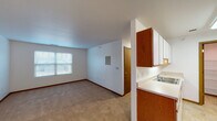 This single-floor unit offers a practical and well-organized layout designed to maximize functionality. The open living area is finished with neutral wall-to-wall carpeting and crisp white walls, creating a clean, versatile backdrop. A window allows natural light to filter into the space, offering views of the surrounding neighborhood. The living area connects seamlessly to the kitchen via a half-wall partition, providing an open sightline between the two spaces.

The galley-style kitchen is efficiently arranged with white cabinetry on both sides, warm wood-trimmed upper and lower cabinets, light countertops, and durable tile-style flooring. White appliances including an electric range and refrigerator are included. A doorway from the kitchen leads to a dedicated pantry or storage room with wire shelving, adding notable storage capacity.

The bedrooms are carpeted and well-lit, each featuring windows with blinds. One bedroom includes a large sliding-door closet, while another offers a generously sized walk-in closet outfitted with wire shelving along multiple walls. The bathroom is thoughtfully designed with accessibility in mind, featuring grab bars near the toilet and walls, a vanity with storage, and light-toned flooring. Overall, the unit presents a clean, functional living environment.