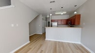 This two-story, 3-bedroom, 3-bathroom residence offers a well-designed layout with consistent light wood flooring and neutral gray tones throughout. The open-concept living and dining area benefits from vaulted, angled ceilings that lend a sense of volume and airiness to the space. Multiple windows and a glass-paneled exterior door flood the living area with natural light and provide views of surrounding greenery.

The kitchen is thoughtfully appointed with rich cherry wood cabinetry, granite-style countertops, a full suite of stainless steel appliances — including a refrigerator, range, microwave, and dishwasher — and a peninsula breakfast bar with pendant lighting overhead. A double-basin sink adds practicality to the space.

Each of the three bedrooms features light wood flooring, neutral wall tones, and sliding mirrored closets, with windows providing natural light. The bathrooms are finished with matching cherry wood vanities and granite-style countertops; one bathroom includes a double-sink vanity with a tub-shower combo, while additional bathrooms offer single-sink vanities with tub-shower combinations. A staircase connects the two floors, and the overall design presents a clean, functional, and comfortable living environment.