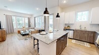 Located at 4961 Springdale Rd in Louisville, KY, this single-floor, 2-bedroom, 2-bathroom residence offers a thoughtfully designed open-concept layout. The kitchen is a standout feature, boasting a granite-topped center island with pendant lighting, two-tone cabinetry combining crisp white upper cabinets with warm wood-grain lower cabinets, stainless steel appliances, and granite countertops throughout. The kitchen flows seamlessly into the bright living room, which is lined with large windows dressed in neutral drapes, flooding the space with natural light and views of the outdoors. Light hardwood flooring runs through the main living areas, adding warmth and continuity. The primary bedroom is a comfortable retreat with plush carpeting, a ceiling fan, and a window allowing natural light. Both bathrooms are finished with granite-topped wood-tone vanities and tiled tub-shower combinations. The second bedroom also features soft carpeting and a natural light source. A dedicated closet and hallway complete the layout. The overall design palette—neutral walls, modern fixtures, and consistent material choices—creates a clean, cohesive, and contemporary living environment.