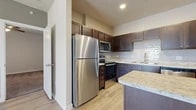 This thoughtfully laid-out one-bedroom, one-bathroom residence features a cohesive design that balances functionality and comfort throughout its single floor. The kitchen is a standout space, showcasing rich dark-espresso cabinetry with ample upper and lower storage, light granite countertops, a tiled subway backsplash, and a full suite of stainless steel appliances including a refrigerator, range, microwave, and dishwasher. A peninsula with a granite surface provides additional prep space and a casual dining option. Light wood-style flooring runs through the kitchen and living areas, lending a clean, contemporary feel. The living room is bright and airy, featuring a ceiling fan with light fixture, neutral gray accent walls, and windows that allow natural light to fill the space. The bedroom offers plush carpeting, a ceiling fan, and a window with outdoor views, creating a comfortable and quiet retreat. A dedicated closet provides convenient storage adjacent to the bedroom. The bathroom is well-appointed with dark cabinetry, a granite-topped vanity, a tub-shower combination with full gray tile surround, and wood-style flooring. Clean white trim and neutral tones are carried consistently throughout the unit, creating a polished and unified aesthetic.