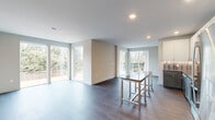 This well-appointed 3-bedroom, 2-bathroom single-story home offers a thoughtfully designed layout that balances comfort and modern style. The open-concept living and kitchen area serves as the heart of the home, featuring wide-plank hardwood flooring, recessed lighting, and large sliding glass doors that flood the space with natural light and provide views of the surrounding greenery. The kitchen is a standout, showcasing two-tone cabinetry with white upper cabinets and grey lower cabinets, granite countertops, a decorative tile backsplash, stainless steel appliances, and a freestanding island with matching granite. A wide hallway with a barn-style sliding door connects the living area to the private quarters. The generously sized primary bedroom offers ample space, while the two additional bedrooms feature plush carpeting and large windows with outdoor views. Two closets provide convenient storage throughout. The bathrooms are finished with clean, modern fixtures, including a walk-in shower with floor-to-ceiling tile and a striking black-framed glass sliding door. Neutral tones and clean lines carry throughout the home, creating a cohesive and contemporary ambiance.