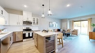 Located at 6470 37th Ave NW in Rochester, MN, this thoughtfully designed one-bedroom, two-bathroom residence offers a highly functional single-floor layout with modern finishes throughout. The open-concept kitchen is a standout feature, equipped with stainless steel appliances, crisp white upper cabinetry, warm wood-toned lower cabinets, a subway tile backsplash, and a central island with a quartz countertop, built-in beverage cooler, and bar seating — all illuminated by stylish pendant lighting. The kitchen flows seamlessly into the living room, where light-toned hardwood floors, neutral walls, and a large sliding glass door create a bright, welcoming atmosphere with outdoor views. The primary bedroom is a comfortable retreat, featuring plush carpet, large windows overlooking a green landscape, and direct access to a spacious walk-in closet with wire shelving on three walls. The two bathrooms are finished with warm wood vanities, white countertops, and clean, contemporary fixtures. Recessed lighting and a consistent neutral color palette unify the space, lending it a polished, modern aesthetic well-suited for everyday living.