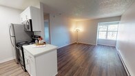 This single-floor unit offers a thoughtfully designed layout that balances functionality and comfort. The open-concept living area is anchored by rich, dark-toned hardwood-style flooring that flows seamlessly from the kitchen into the main living space, creating a cohesive and inviting atmosphere. Neutral gray walls and a textured ceiling complement the warm tones of the flooring, while a window allows natural light to brighten the room.

The galley-style kitchen is efficiently laid out with crisp white cabinetry extending to the ceiling for generous storage, white quartz countertops, and a full suite of stainless steel appliances including a refrigerator, microwave, electric range, and dishwasher. A peninsula counter with additional seating and prep space connects the kitchen to the living area.

The bedroom offers a calm retreat with plush wall-to-wall carpeting, a window with garden views, and a baseboard heating unit. An open closet provides convenient storage. The bathroom features a white quartz vanity with an undermount sink, brushed nickel fixtures, a full-width mirror, and a shower-tub combination. The space is finished with clean, modern touches throughout, making it a practical and comfortable place to call home.