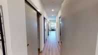Unit C219 is a thoughtfully designed single-floor residence located at 24975 Frager Rd S in Kent, Washington. The layout is organized around a central hallway finished with light wood-look flooring and crisp white walls, connecting each area of the unit seamlessly. Recessed lighting runs the length of the corridor, lending a clean, contemporary feel from the moment you enter.

The living area is a welcoming space anchored by a large window that draws in natural light and offers views of the surrounding neighborhood. Light wood-tone flooring continues here, complementing the neutral walls and providing a warm, modern aesthetic.

The kitchen is well-appointed with white flat-front cabinetry, gray quartz-style countertops, a subway tile backsplash, and stainless steel appliances including a dishwasher and range. A sizable window above the dining area adds brightness and an outward view.

The bedroom is a calm, comfortable retreat accessed via a sliding barn door, adding a contemporary architectural detail. Neutral carpet, soft lighting, and clean lines create a restful atmosphere.

The bathroom features a gray countertop vanity with an undermount sink, a full mirror, built-in shelving, and a shower-tub combination with a curtain rod. The finishes throughout maintain the unit's consistent modern palette of whites, grays, and warm wood tones.