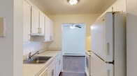 This single-floor unit offers a practical and efficiently designed layout, accommodating two bedrooms, a living room, a kitchen, a dedicated closet, and two hallways within its compact footprint. The galley-style kitchen is fitted with white cabinetry above and below the counters, a stainless steel sink, white appliances including a refrigerator and range, and durable hardwood-style flooring. Upper and lower cabinet storage provides functional organization, and a doorway opening connects the kitchen directly to the living area.

The living room features a ceiling fan, baseboard heating, and a large sliding glass door dressed with vertical blinds that invites an abundance of natural light. The flooring transitions from hardwood-style near the kitchen to plush carpet in the main seating area, creating a warm, comfortable atmosphere.

Both bedrooms are carpeted and include built-in closets with shelving for organized storage. The primary bedroom is generously sized relative to the overall footprint, with a window providing natural light and baseboard heating for year-round comfort. The second bedroom also features a closet with shelving. The neutral white walls throughout the unit create a clean, bright aesthetic that complements the functional design.