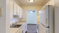 This single-floor unit offers a practical and efficiently designed layout, accommodating two bedrooms, a living room, a kitchen, a dedicated closet, and two hallways within its compact footprint. The galley-style kitchen is fitted with white cabinetry above and below the counters, a stainless steel sink, white appliances including a refrigerator and range, and durable hardwood-style flooring. Upper and lower cabinet storage provides functional organization, and a doorway opening connects the kitchen directly to the living area.

The living room features a ceiling fan, baseboard heating, and a large sliding glass door dressed with vertical blinds that invites an abundance of natural light. The flooring transitions from hardwood-style near the kitchen to plush carpet in the main seating area, creating a warm, comfortable atmosphere.

Both bedrooms are carpeted and include built-in closets with shelving for organized storage. The primary bedroom is generously sized relative to the overall footprint, with a window providing natural light and baseboard heating for year-round comfort. The second bedroom also features a closet with shelving. The neutral white walls throughout the unit create a clean, bright aesthetic that complements the functional design.