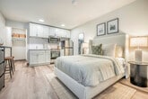 Located at 4765 Hayes Rd in Madison, Wisconsin, this efficiently designed studio unit offers a thoughtfully organized open-plan layout across a single floor. Light wood-look flooring flows throughout, complementing the clean, neutral color palette that gives the space a bright and airy feel.

The main living area seamlessly integrates the sleeping, dining, and kitchen functions. The kitchenette is outfitted with white shaker-style cabinetry extending to the ceiling, marble-look countertops, and a full suite of stainless steel appliances, including a refrigerator, range with oven, and built-in microwave. A compact dining area with a bar-height table and stools provides a dedicated spot for meals.

The sleeping area is anchored by a generously sized bed with an upholstered headboard, flanked by bedside lamps that contribute to the warm, restful ambiance. A full-length mirror and framed wall art add character to the space.

Two bathrooms serve the unit — one features a walk-in shower with built-in shelving and wood-look tile flooring, while the other includes a vanity with ample under-cabinet storage and an adjacent open closet with shelving and a hanging rod for added organization. Recessed lighting throughout ensures consistent illumination across the entire unit.