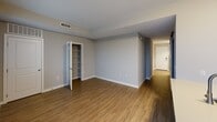 Located at 2827 Telek Pl, Unit 1203, in Alexandria, Virginia, this efficiently designed single-floor unit offers a well-organized layout that makes thoughtful use of its intimate footprint. The space is composed of a hallway entry and a kitchen, with an open living area visible from both zones.

The kitchen is a standout feature, showcasing contemporary dark espresso-toned cabinetry that extends to the ceiling for maximum storage. Stainless steel appliances — including a refrigerator, electric range, and over-the-range microwave — complement the clean, white quartz countertops. A peninsula island with an undermount sink and additional electrical outlets provides both prep space and a casual dining option. A tiled backsplash adds a refined finishing touch, while a large window floods the kitchen with natural light.

The open living area is finished with warm hardwood-style flooring that runs throughout, neutral gray walls, and clean white trim and baseboards. A built-in shelving unit with a glass-paned door offers convenient storage. The hallway connects the main living space to the entry door and bathroom area, maintaining a logical and efficient flow. Ceiling vents are well-integrated throughout, ensuring consistent climate control. The overall aesthetic is modern and move-in ready.