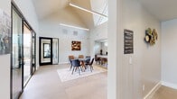 This single-story community clubhouse is designed with a clean, contemporary aesthetic, highlighted by dramatic vaulted ceilings with skylights that flood the interior with abundant natural light. Large-format neutral tile flooring runs throughout, lending a cohesive and polished look to the entire space.

The main gathering area serves as the heart of the clubhouse, featuring multiple seating arrangements including a concrete-top dining table with mixed leather and upholstered chairs, as well as a pair of cognac leather lounge chairs accented by curated abstract wall art. A wall-mounted flat-screen TV and a decorative sideboard add functional style to this communal zone.

Adjacent to the main area, a fully equipped kitchen is outfitted with a textured tile backsplash, stainless steel appliances, a breakfast bar with counter seating, and clerestory windows that bring in additional natural light.

A dedicated business center, enclosed by sleek glass-panel walls with black metal frames, provides workstations with computers and a printer, offering a quiet and professional environment. A reception area is also accessible through glass-framed doors.

The space opens directly to a covered outdoor patio featuring a warm wood-paneled ceiling, pendant lighting, and comfortable teal seating overlooking a resort-style pool and deck area — creating a seamless indoor-outdoor living experience.
