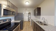 Located at 2591 Venturi House in Columbus, Ohio, this single-floor residence offers a well-designed layout with contemporary finishes throughout. The kitchen is a standout feature, showcasing dark espresso cabinetry, granite countertops, white subway tile backsplash, and a full suite of stainless steel appliances including a range, microwave, refrigerator, and dishwasher. Wood-look flooring runs through the kitchen, which opens via a peninsula into the living area — a generous, carpet-floored space with a ceiling fan and direct sightlines to the kitchen. A dedicated laundry area with washer and water heater is conveniently accessible from the kitchen. The bedrooms are carpeted and finished with neutral gray walls, offering a calm and comfortable atmosphere. Windows allow natural light to filter in, and at least one bedroom features a built-in closet with shelving. The bathrooms are well-appointed, with granite-topped dark vanities, framed mirrors, and wood-look flooring. One full bathroom includes a tub-shower combo, while a second half or three-quarter bath provides additional convenience. The overall design is cohesive and modern, making this a functional and attractive single-level residence.