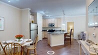 This single-floor, 2-bedroom, 1-bathroom residence offers a thoughtfully designed layout that makes efficient use of its space. The open-concept kitchen and living area serves as the heart of the home, featuring light maple cabinetry, dark granite countertops, and a full suite of stainless steel appliances including a refrigerator, electric range, and built-in microwave. A curved kitchen island with pendant lighting provides additional prep space and casual bar seating. Warm hardwood-style flooring flows throughout the main living areas, complemented by crown molding that adds a refined architectural touch. The living room is bright and welcoming, with sheer curtain-framed windows that allow natural light to filter in. The generously sized primary bedroom features plush carpeting, a ceiling fan, and windows with sheer drapes, creating a calm and restful atmosphere. The second bedroom is similarly appointed, offering comfortable proportions and a ceiling fan. The full bathroom is finished with tile flooring, a wood-toned vanity with a stone countertop, and a shower-tub combination. A dedicated closet and hallway complete the floor plan, providing practical storage and easy circulation throughout the residence.