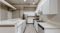 Located at 315 Commerce Ave SW in the heart of downtown Grand Rapids, Michigan, this two-bedroom, two-bathroom unit blends industrial loft character with modern updates. The space is defined by its soaring ceilings with exposed ductwork and structural elements, whitewashed brick accent walls, and light luxury vinyl plank flooring throughout the main living areas.

The kitchen is well-appointed with crisp white cabinetry, speckled stone countertops, a peninsula with additional prep space, and a full suite of stainless steel appliances including a refrigerator, range, microwave, and dishwasher. Track lighting illuminates the space, enhancing its open, airy feel.

Both bedrooms feature plush carpet flooring and large windows with vertical blinds that allow ample natural light. The exposed brick walls carry through into the bedrooms, reinforcing the industrial aesthetic. The generously sized primary bedroom offers a comfortable and private retreat.

The two bathrooms are finished in a clean, neutral palette. One features a full soaking tub and shower combination, while the other offers a dedicated walk-in shower stall, providing practical flexibility for residents. Light wood-tone flooring ties each bathroom together seamlessly.

A hallway connects the rooms efficiently, and the overall layout, as seen in the 3D model, offers a well-organized and functional flow throughout the single-floor unit.