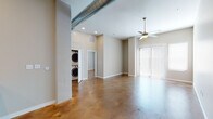 This single-floor unit showcases a contemporary industrial-modern aesthetic anchored by richly stained, polished concrete floors that run throughout every room, lending warmth and a distinctive character to the space. The open-concept layout connects the living area and kitchen seamlessly, creating an expansive, airy feel enhanced by tall ceilings and recessed lighting.

The kitchen is well-appointed with white shaker cabinetry, light quartz countertops, a subway tile backsplash, and a full suite of stainless steel appliances including a range, over-the-range microwave, and refrigerator. A peninsula with an integrated sink provides additional prep space and defines the transition between the kitchen and living area.

The generous living space features an exposed ductwork detail along the ceiling, adding an industrial touch, alongside a ceiling fan and access to natural light through large windows fitted with vertical blinds. The bedroom is comfortable and well-lit, with windows offering natural light, a ceiling fan, and access to a mirrored bathroom featuring white cabinetry, quartz countertops, brushed nickel fixtures, and a tiled shower. A dedicated laundry closet with a stacked washer and dryer adds everyday convenience. Neutral wall tones throughout create a clean, cohesive backdrop.