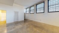 This one-bedroom, one-bathroom residence at 9380 Quadrangle St, Unit 102 in Lorton, Virginia showcases a distinctive industrial-chic aesthetic that sets it apart. Throughout the main living area and kitchen, polished concrete floors reflect natural light streaming in through oversized grid-style windows framed in sleek black — a nod to the building's industrial heritage. Painted white brick walls add texture and character while maintaining a bright, clean atmosphere.

The open-concept kitchen is well-appointed with rich dark wood cabinetry, granite countertops, and stainless steel appliances including a refrigerator, range, and built-in microwave. A peninsula with a granite overhang provides additional workspace and casual seating.

The bedroom offers a change in ambiance, featuring plush wall-to-wall carpet, a painted brick accent wall, and large grid windows that bring in abundant natural light. The room connects directly to a generously sized walk-in closet outfitted with wire shelving, offering ample storage.

The full bathroom is clean and functional, featuring a granite-topped vanity with dark wood cabinetry, a shower/tub combination, and polished concrete flooring consistent with the unit's modern aesthetic. Recessed lighting throughout ensures well-lit interiors, while the overall layout makes efficient use of the available space.