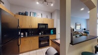 This single-floor residence offers a thoughtfully designed layout that balances functionality and comfort across several distinct living spaces. The kitchen is a standout feature, equipped with flat-front maple cabinetry extending to the ceiling, dark granite countertops, a bold black tile backsplash, and a full suite of black appliances including a refrigerator, oven, microwave, and dishwasher. Light tile flooring runs throughout the kitchen, which connects seamlessly to the rest of the unit.

The living area features rich wood-look flooring and receives natural light through a sliding glass door that opens to a private balcony with outdoor views. The space accommodates both a seating area and additional furnishing with ease.

A versatile secondary room, carpeted and bright, benefits from tall windows overlooking outdoor scenery, making it well-suited as a home office or flex space. The primary bedroom is generously proportioned with plush carpet, a ceiling fan, and a large window framing outdoor views, creating a calm retreat.

The bathroom is finished with tile flooring, a dark granite vanity with maple cabinetry, a tub-shower combination, and a tall storage cabinet, offering practical storage solutions throughout.