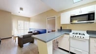 Located at 1091 Everton Place in Riverside, CA, this single-story unit offers a practical and well-organized layout with two bedrooms and two full bathrooms. Light wood-style flooring runs throughout the space, creating a clean, cohesive look.

The kitchen is efficiently designed with white cabinetry, gray stone-look countertops, a gas range, refrigerator, and over-the-range microwave. A skylight overhead brightens the space, while a peninsula with bar seating connects the kitchen to the living area, creating an open, social flow.

The living room features a two-tone wall design with a bold blue lower half and warm beige upper half, adding a distinctive visual element. Vertical blinds along the window allow natural light to filter in. The space comfortably accommodates seating and a television setup.

The primary bedroom offers a generous, open layout with a window and vertical blinds providing natural light. The second bedroom is configured for shared occupancy, featuring built-in bunk bed frames with integrated desks and shelving on each side — ideal for a collegiate or co-living setting — along with a window with outdoor views.

Both bathrooms are similarly appointed, each featuring a tub-shower combination with sliding glass doors, a single-sink vanity with stone-look countertops, and light flooring. A dedicated closet rounds out the unit's storage offerings.