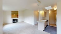 Located at 1110 E Cozza Dr in Spokane, Washington, this single-floor unit offers a well-organized layout with a clean, neutral aesthetic throughout. The open-concept living and dining area is generously sized, featuring soft wall-to-wall carpeting, vaulted ceilings with track lighting, and a tile-surround fireplace that serves as a focal point. A large window fills the space with natural light and frames views of the surrounding greenery, while baseboard heating ensures year-round comfort.

The kitchen is positioned adjacent to the living area and features a peninsula breakfast bar, light wood cabinetry, a skylight that brightens the workspace, and a full suite of appliances including a refrigerator and stove. The open pass-through design connects the kitchen seamlessly to the main living space.

The bedrooms are carpeted and comfortably proportioned, each with windows offering outdoor views and access to natural light. The primary bedroom includes a built-in vanity with mirror and a walk-in closet. A window-mounted air conditioning unit provides supplemental cooling.

The bathroom is finished with tile flooring, a wide vanity with ample counter space and storage, and a full soaking tub with a tiled surround. The overall interior palette of soft whites and warm neutrals lends the space a bright, airy feel throughout.