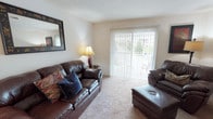 This classic three-bedroom, two-bathroom residence is thoughtfully laid out across a single floor, offering a functional and comfortable living environment. The living room serves as the heart of the home, featuring plush carpeting, neutral walls, and a sliding glass door flanked by vertical blinds that opens to an outdoor patio, flooding the space with natural light and providing views of the surrounding greenery.

Adjacent to the living room, a dedicated dining area features two-tone painted walls, a chandelier overhead, and ample space for a full dining set. The kitchen is equipped with warm oak cabinetry, dark countertops, a double-basin sink, and white appliances including a range and dishwasher, complemented by tile flooring.

The primary bedroom offers carpeted floors and generous storage, while a second bedroom provides a bright, welcoming retreat with a window and soft carpet. Both bathrooms feature white vanities with storage cabinetry, mirrored medicine cabinets, and tub-shower combinations. The overall aesthetic throughout is classic and understated, with neutral tones creating a cohesive and move-in-ready atmosphere.
