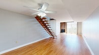 Located at 2350 Timberview Rd in Kirkwood, Missouri, this two-story residence offers a thoughtfully designed layout with consistent hardwood flooring throughout both levels. The main living area is generously proportioned, highlighted by a striking corner fireplace set against a wood-paneled accent wall. Large sliding glass doors flood the space with natural light and provide outdoor views, while a ceiling fan adds functional comfort overhead.

A standout architectural feature is the open-riser staircase constructed with rich wood treads and black metal railings, creating a visually dynamic connection between the two floors. The upper level opens to a bright loft-style landing with wood-and-iron railings overlooking the main living space below, benefiting from abundant natural light through large windows.

The kitchen is efficiently laid out with warm honey-toned wood cabinetry, granite-style countertops, and black appliances including a refrigerator, range, and dishwasher. A pass-through window connects the kitchen to an adjacent living or dining area, enhancing the open feel of the home.

A lower-level bedroom features dual closets and soaring double-height ceilings, with a mezzanine-style upper area visible above, reinforcing the home's open, airy character throughout.