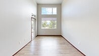 Located at 3928 Northwest Ave, this single-floor unit offers a thoughtfully designed layout that maximizes its compact footprint. The living area immediately impresses with soaring double-height ceilings and a stacked window arrangement—a transom above a standard window—that floods the space with natural light while framing views of surrounding trees and open sky. Light wood-look flooring runs throughout the main living areas, complemented by rich dark wood trim and baseboards that add warmth and contrast.

The kitchen is a standout feature, equipped with rich dark cabinetwood cabinetry, mosaic tile backsplash, white quartz countertops, and a full suite of stainless steel appliances including a refrigerator, range, microwave, and dishwasher. A center island provides additional prep and dining space. Adjacent to the kitchen, a dedicated laundry area houses a stacked washer and dryer, while a built-in shelving unit offers additional storage.

The carpeted bedroom is quietly tucked away with access to a closet featuring built-in shelving. The bathroom features wood-look flooring, a vanity with quartz countertop, and a grab bar. A glass-paneled entry door completes the space, enhancing the airy, open ambiance throughout.