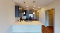 This single-floor unit offers a thoughtfully designed layout that balances open communal spaces with comfortable private quarters. The kitchen serves as a centerpiece of the living area, showcasing striking navy blue shaker-style cabinetry paired with crisp white quartz countertops. A large peninsula with an undermount sink and built-in outlets provides generous prep space and casual seating, while pendant lighting adds a stylish accent overhead. Stainless steel appliances, including a French door refrigerator, electric range, and built-in microwave, complete the kitchen's modern, functional aesthetic. Recessed lighting and a tile backsplash further elevate the space. Rich, warm-toned hardwood-style flooring runs throughout the entire unit, creating a cohesive and inviting atmosphere. The bedroom is a well-proportioned retreat, featuring a ceiling fan and clean neutral walls that offer a calm, restful environment. An adjacent full bathroom is outfitted with a soaking tub and shower combo with white tile surround, a toilet, and a vanity. A doorway from the bathroom leads directly into a dedicated walk-in closet with built-in shelving and drawer units, providing ample and organized storage. The overall design is clean, modern, and move-in ready.