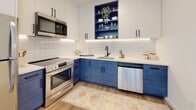 Located at 2913 W Leigh St in Richmond, Virginia, this single-floor unit offers a clean, contemporary design with a cohesive aesthetic carried throughout each space. Light-toned luxury vinyl plank flooring runs consistently across the open living and bedroom areas, contributing to a bright, airy feel that is further enhanced by large black-framed windows overlooking mature trees and the surrounding neighborhood.

The open-concept living and kitchen area is a standout feature of the unit. The kitchen is thoughtfully designed with bold navy lower cabinetry paired with white upper cabinets, a white tile backsplash with under-cabinet LED lighting, stainless steel appliances including a range, microwave, and dishwasher, and a matte black faucet at the sink. A built-in open shelving niche, finished in matching navy, adds a distinctive design element.

The bedroom is generously proportioned, featuring recessed lighting, a pendant fixture, and a large window that frames outdoor greenery, creating a calm and inviting atmosphere.

The bathroom is well-appointed with terrazzo tile flooring, a full tub-shower combination with white subway tile surround, a built-in niche, a modern blue vanity with a white countertop, and matte black hardware and fixtures throughout.