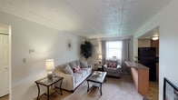 This single-floor residence offers a thoughtfully arranged layout designed for comfortable everyday living. The living room serves as the heart of the space, featuring carpet flooring, a textured ceiling, and a window that brings in natural light. The open arrangement accommodates both a seating area and a defined dining space, where a bar-height table and stools sit adjacent to the living area, creating a seamless flow between the two zones.

The kitchen is well-equipped with warm oak cabinetry, dark granite-style countertops, and a full suite of black appliances, including a refrigerator, electric range, dishwasher, and built-in microwave. Tile flooring and flush-mount lighting complete the practical, efficient design.

Both bedrooms are carpeted and share a consistent aesthetic, each featuring a ceiling fan with integrated lighting, windows with curtain panels, and ample space for furnishings. The rooms offer a calm, restful atmosphere well-suited for relaxation.

The bathroom is cleanly finished with tile flooring, a single-sink vanity with wood cabinetry, and a tub-shower combination enclosed by a striped fabric curtain. A flush-mount ceiling light provides even illumination throughout. Overall, the space presents a neutral, functional, and comfortable environment.