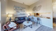 Located at 4816 McMahon Blvd NW in Albuquerque, New Mexico, this one-bedroom, one-bathroom unit offers a smartly designed single-floor layout that maximizes every square foot. The open-concept living area features light wood-look flooring, neutral warm-toned walls, and a seamless flow between the living room and kitchen. The kitchen includes a bar-height counter with seating for two, a stainless steel sink, and a mirrored backsplash that adds depth to the space. A large sliding glass door in the living area opens to a private balcony overlooking lush tree canopies, filling the interior with natural light and outdoor views. The bedroom is generously proportioned, accommodating a queen-sized bed with ease, and includes a mirrored sliding-door closet that enhances the sense of space. A round wall mirror and natural light from a window further brighten the room. The bathroom features a full tub-shower combination with clean white tile, wood-look flooring, and crisp, bright finishes throughout. The unit's cohesive neutral palette, modern fixtures, and thoughtful layout make it a well-appointed and functional living space.