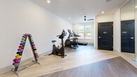 Located at 565 Cobb Pkwy S in Marietta, Georgia, this fitness room offers a well-organized and functional workout space designed to accommodate a variety of exercise routines. The room features durable wood-look flooring throughout, crisp white walls, and recessed lighting complemented by a sleek black ceiling fan that promotes air circulation during workouts.

Natural light filters in through a large window, creating a bright and inviting atmosphere. A full-length wall mirror on one side of the room enhances the sense of openness while allowing users to monitor their form during exercise.

The space is outfitted with a practical selection of cardio equipment, including a treadmill, an elliptical trainer, and a stationary bike, all positioned to allow comfortable use. A color-coded dumbbell rack lines one wall, offering a range of free weight options alongside a set of stability and exercise balls displayed on a dedicated rack. Additional fitness accessories are conveniently stored within the room.

Two navy blue doors provide access points to and from the space, contributing a bold design accent against the neutral walls. Overall, this fitness room delivers a clean, modern environment with all the essential equipment needed for a comprehensive workout, making it a convenient and accessible amenity.
