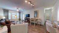 This single-floor residence offers a thoughtfully designed open-concept layout that seamlessly connects the living, dining, and kitchen areas. The living room is a welcoming space, featuring rich hardwood-style flooring, a ceiling fan, and large windows dressed with patterned drapes that invite natural light while maintaining privacy. A dedicated seating area with a sectional sofa, glass coffee table, and track lighting overhead creates a comfortable and functional gathering space.

The kitchen is a standout feature, showcasing rich dark cabinetry paired with granite-style countertops, stainless steel appliances, a double sink, and pendant lighting above a breakfast bar with seating — ideal for casual dining. A separate dining nook provides additional space for entertaining.

Each bedroom is carpeted and serene, offering a tranquil retreat with ample natural light. The primary bedroom features soft neutral tones and generous space, while the secondary bedroom is equally well-appointed with a cozy, inviting atmosphere.

The bathrooms are finished with tile flooring, dark wood vanities with granite-style countertops, and well-lit mirrors. One bathroom features a bold navy accent wall, adding a touch of sophisticated contrast. Throughout the residence, the consistent use of quality finishes and cohesive design elements contribute to a polished, comfortable living environment.