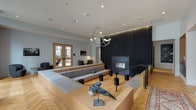 This elegantly designed single-floor amenity space offers a seamless blend of modern architecture and warm, curated interiors throughout its interconnected zones. The centerpiece is a dramatic sunken lounge anchored by a floor-to-ceiling dark wood accent wall and a sleek linear fireplace, with a large wraparound bench seating area and an eye-catching sculptural chandelier overhead. Recessed lighting and ambient LED strips enhance the refined atmosphere throughout.

The full kitchen features a generous island with a dark stone countertop and sculptural wood barstools, set against rich metallic cabinetry and warm wood shelving. Globe pendant lights and herringbone hardwood flooring — a consistent detail across the entire space — tie the aesthetic together. A dedicated coffee and beverage station provides a self-serve nook with professional-grade equipment.

Adjacent areas include a comfortable lounge with oversized sectional seating and floor-to-ceiling windows that flood the room with natural light, as well as a billiards room with ample overhead lighting. A formal dining area features a long wood banquet table with leather booth seating and a large mirror. A transitional hallway showcases a striking built-in geometric bookshelf in dark metal, complemented by a vintage-style area rug. Double oak doors open to an outdoor terrace, completing this well-appointed communal space.