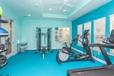 Located on Summerwood Drive in Clarkston, Georgia, this fitness center is a thoughtfully designed single-floor facility built to support a comprehensive workout experience. The space is defined by its vibrant teal flooring and dual-tone teal and light blue walls, creating an energetic yet clean aesthetic throughout.

Natural light floods the room through multiple white-framed windows dressed with horizontal blinds, offering views of the surrounding greenery and maintaining a connection to the outdoors. Recessed lighting and a tray ceiling add architectural depth and ensure the space is well-lit at all times.

The facility is equipped with a diverse range of exercise equipment. Cardio offerings include a treadmill, elliptical, stationary bike, and rowing machine. A multi-functional cable machine paired with a flat bench supports strength training, while a tiered dumbbell rack provides free weight options across varying sizes. Additional functional fitness tools such as medicine balls, BOSU balls, and kettlebells are neatly organized on a dedicated storage rack.

A set of glass French doors connects to an adjacent room that appears to contain a sink or restroom area, adding practical convenience. The overall layout is open and organized, making the space accessible and functional for a variety of fitness routines.