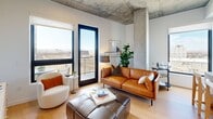 Located on Blake Street in Denver's vibrant RiNo neighborhood, this contemporary residence blends industrial and modern design throughout its single-floor layout. Exposed concrete ceilings and structural columns serve as defining architectural elements, contrasting elegantly with crisp white walls and warm light wood flooring found throughout the space.

The open-concept kitchen is well-appointed with stainless steel appliances, two-tone cabinetry in light wood and dark finishes, a large waterfall-edge island with bar seating, and black matte fixtures. Natural light pours in through black-framed windows that frame sweeping Denver skyline views. The living area connects directly to a private balcony, extending the space outdoors.

Multiple bedrooms each feature black-framed windows with city or neighborhood views and exposed concrete ceilings that reinforce the industrial character. One bedroom includes an en-suite bathroom with a walk-in closet, a wide vanity with light wood cabinetry, white countertops, and matte black hardware. A second full bathroom offers a soaking tub, large-format tile flooring, and a generous vanity. The overall ambiance is clean, modern, and sophisticated, with an urban edge.