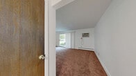 This 2-bedroom, 1-bathroom residence at 920 E Robinson Rd in North Tonawanda, NY offers a clean, functional layout across a single floor. The interior is finished with crisp white walls and bright trim throughout, creating a light and airy atmosphere. Light-toned luxury vinyl plank flooring runs through the main living areas, including the combined kitchen and living room, dining room, and bathroom, while plush carpeting covers both bedrooms.

The kitchen features white raised-panel cabinetry extending to the ceiling for ample storage, light-toned countertops, and white appliances including a refrigerator and electric range. Adjacent to the kitchen, the dining area is defined by a stylish dark pendant chandelier overhead. The living room connects seamlessly to these spaces, offering an open and cohesive common area.

Both bedrooms are generously proportioned with neutral carpet, white walls, and baseboard heating. The primary bedroom includes a wall-mounted air conditioning unit for year-round comfort. Windows in the bedrooms admit natural light and offer views of the surrounding greenery. The full bathroom is clean and bright, featuring a tub-shower combination, vanity with white cabinetry, and light plank flooring. A central hallway connects all rooms efficiently, completing this well-organized and move-in-ready home.
