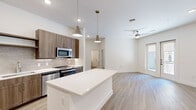 Located in Richardson, TX, this thoughtfully designed 2-bedroom, 3-bathroom residence offers a well-appointed single-floor layout. The open-concept kitchen and living area serves as the heart of the home, showcasing warm wood-toned cabinetry, a tile backsplash, stainless steel appliances, and a large central island with a crisp white countertop. Stylish pendant lighting and recessed fixtures illuminate the space, while light wood-look flooring extends throughout the main living areas. A ceiling fan adds comfort to the airy living room, which receives natural light through a nearby window. The two bedrooms feature plush carpeting and bright neutral walls; one bedroom includes a window with an outdoor view, while the primary bedroom connects to a well-organized walk-in closet with multi-level shelving and hanging rods. The bathrooms are finished with marble-style tiled tub-and-shower surrounds with built-in niches, wood-toned vanities, and light flooring for a clean, modern aesthetic. A dedicated laundry room houses a full-size front-load washer and dryer. Two closets provide ample storage throughout the residence, rounding out a functional and contemporary living experience.