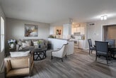 This single-floor unit is designed with an open-concept layout that seamlessly connects the living area and kitchen, creating a functional and cohesive living space. Wood-look flooring runs throughout, providing a warm, consistent foundation underfoot.

The living area is well-proportioned, offering room for comfortable seating arrangements. A window allows natural light to filter in, brightening the neutral-toned walls. The space opens directly toward the kitchen, which is defined by a half-wall peninsula with a dark countertop. The kitchen features white cabinetry extending to the upper walls, providing ample storage, alongside white appliances including a refrigerator, electric range, and built-in ventilation hood.

The bedroom is a calm retreat finished in the same wood-look flooring, with a window fitted with blinds for light control. A ceiling fan overhead adds comfort and airflow to the room.

The bathroom includes a full tub and shower combination with white tile surround, a vanity with storage, and matching wood-look flooring that ties the space together. The entry area features a solid front door with a sidelighting window, providing a welcoming and secure point of access into the unit.