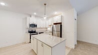 This single-floor unit at 2486 120th Ave in Holland, Michigan, presents a clean, modern aesthetic throughout its well-designed layout. The kitchen serves as a standout feature, showcasing white shaker-style cabinetry, light quartz countertops, and a classic subway tile backsplash. A central island provides additional prep and seating space, while stainless steel appliances—including a range, microwave, dishwasher, and refrigerator—complete the functional setup. Light hardwood-style flooring runs throughout the kitchen, lending a bright, airy feel.

The living area is generously proportioned, with vaulted ceilings, recessed lighting, and a distinctive green entry door framed by windows that invite natural light. Plush carpeting extends into the bedrooms, each equipped with ceiling fans and ample windows. One bedroom features an attached en-suite bathroom, while additional bedrooms offer closet space and comfortable proportions.

The bathrooms are finished with white cabinetry, light countertops, and hardwood-style flooring. One bathroom includes a full tub-shower combination with brushed nickel fixtures, while the en-suite features a spacious vanity with a large mirror. The overall palette of whites and neutrals creates a cohesive, move-in-ready environment throughout.