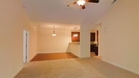 Located at 1141 Glen Iris Dr in Fayetteville, North Carolina, this single-story home offers a thoughtfully designed open-concept layout that seamlessly connects the living, dining, and kitchen areas. The living space is finished with plush carpeting that transitions into a hard-surface dining area, creating a natural visual distinction between the two zones while maintaining an airy, cohesive feel throughout.

A ceiling fan with an integrated light fixture anchors the living room, providing both comfort and functionality. The dining area is elegantly lit by a pendant light, while a matching chandelier-style fixture above the kitchen bar adds a warm, inviting ambiance to the space.

The kitchen is visible through a raised bar-height counter, which serves as both a practical workspace and a casual dining option. Rich, dark cabinetry provides a striking contrast against the neutral walls and lighter countertops, giving the kitchen a polished and contemporary look. A glimpse into the kitchen corridor reveals ample cabinetry and counter space, suggesting a well-equipped cooking environment.

Throughout the home, soft neutral wall tones and consistent trim work create a clean, welcoming atmosphere. The open sightlines across the main living areas enhance the sense of space, making this single-floor home feel expansive and comfortable for everyday living.
