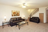 This two-story residence offers a practical and comfortable layout spread across two floors connected by a staircase with metal railings. The main level welcomes you through a front entry into a spacious carpeted living room, complete with a ceiling fan and baseboard heating. The living room provides ample seating space and flows naturally into a bright dining area featuring hardwood-style flooring and a large window that brings in natural light. The galley-style kitchen is efficiently designed with white cabinetry, generous counter space, a full suite of appliances including a refrigerator, electric range, and built-in microwave, all set above warm hardwood-style flooring. A bathroom on the main level features a vanity and toilet in a clean, neutral finish. Upstairs, the second floor hosts multiple carpeted bedrooms, each equipped with ceiling fans and windows that allow natural light. The bedrooms offer generous floor space, with one featuring a sliding closet and an additional mirror dresser setup. A full bathroom on the upper level includes a bathtub and shower combination. Throughout the home, warm neutral tones and consistent ceiling fans in each room contribute to a cohesive, comfortable ambiance suited for everyday living.