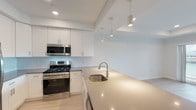 Located at The Channel Club in Island Park, NY, this single-floor residence offers a clean, contemporary design with an open, airy layout. The kitchen is a standout feature, showcasing white shaker cabinetry extending to the ceiling, a classic subway tile backsplash, and a suite of stainless steel appliances including a gas range, built-in microwave, and full-size refrigerator. A generous quartz-topped peninsula with an undermount sink and stylish pendant lighting anchors the space, seamlessly connecting the kitchen to the living area. Light-toned wood flooring runs throughout the main living spaces, enhancing the bright, cohesive atmosphere. The living area is bathed in natural light courtesy of expansive floor-to-ceiling windows with exterior views. The bedroom is well-appointed with a dedicated closet and recessed lighting, while an additional closet provides ample storage. The bathroom features neutral tile flooring, a white vanity with an integrated sink, and a mirrored medicine cabinet for a polished finish. A stacked in-unit washer and dryer adds everyday convenience. Recessed lighting and a tray ceiling detail in the main living area contribute to the refined, modern character of this well-designed residence.