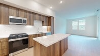 Located at 1205 Aviara Parkway in Carlsbad, CA, this thoughtfully designed one-bedroom, one-bathroom residence offers a well-appointed single-floor layout with a clean, contemporary aesthetic throughout.

The kitchen serves as the centerpiece of the home, showcasing rich walnut-toned cabinetry that extends to the ceiling for ample storage, a striking marble-veined quartz backsplash, and matching quartz countertops. A generous island with a waterfall edge provides additional prep space and casual seating. Stainless steel appliances — including a gas range, built-in microwave, French door refrigerator, and dishwasher — complete this high-end culinary space.

The open living area flows naturally from the kitchen, featuring light wood-tone flooring and large windows that invite abundant natural light and offer pleasant greenery views. A sliding glass door leads to a private balcony, further enhancing the connection to the outdoors.

The bedroom is a bright, serene retreat with dual windows framing lush tree views. It includes access to a dedicated walk-in closet equipped with built-in shelving and hanging rods for organized storage.

The bathroom features large-format tile flooring, a walnut vanity with quartz countertop, a wide mirror, and modern fixtures, maintaining the cohesive design language found throughout the residence.