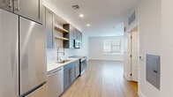 Located at Highline in Littleton, Colorado, this well-designed studio offers a thoughtfully utilized single-floor layout. The open-concept kitchen and living area serves as the heart of the space, where the kitchen stands out with sleek gray shaker-style cabinetry, open wood shelving, a white quartz countertop, and a classic subway tile backsplash. A full suite of stainless steel appliances — including a refrigerator, electric range, over-the-range microwave, and dishwasher — ensures a fully functional cooking experience. Light wood-tone flooring flows seamlessly throughout, enhancing the bright, clean aesthetic. Recessed lighting illuminates the kitchen and living areas, while a large window fitted with horizontal blinds fills the living space with natural light and offers views of the surrounding landscape. The bathroom mirrors the home's contemporary design with matching gray cabinetry, a white countertop vanity, and wood-look flooring. A dedicated laundry area includes a stacked washer and dryer unit alongside shelving and a hanging rod for added storage convenience. Crisp white walls and modern finishes throughout create a cohesive, move-in-ready environment.