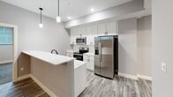 Located at 1230 Elm St in Manchester, NH, this thoughtfully designed 2-bedroom, 1-bathroom residence offers a comfortable and modern living experience across a single floor. The space is laid out with a practical hallway connecting the key rooms, maintaining a clean and organized flow throughout.

The kitchen is a standout feature, showcasing white shaker-style cabinetry extending to the ceiling for generous storage, elegant marble-look quartz countertops, and a full suite of stainless steel appliances including a refrigerator, electric range, and built-in microwave. A peninsula with a waterfall-edge countertop and pendant lighting adds a stylish focal point, while wood-look tile flooring completes the polished aesthetic.

Both bedrooms are finished with patterned carpet, neutral gray walls, and recessed lighting, creating a calm and restful atmosphere. Each room features a window with blinds for natural light, and the primary bedroom includes access to a dedicated closet with built-in shelving. The secondary bedroom also benefits from its own closet space.

The full bathroom is finished with wood-look tile flooring, a full tub-shower combination with clean white surrounds, and matte black fixtures and hardware that add a modern, cohesive touch. The overall design palette of soft grays and whites gives the entire residence a fresh, contemporary feel.